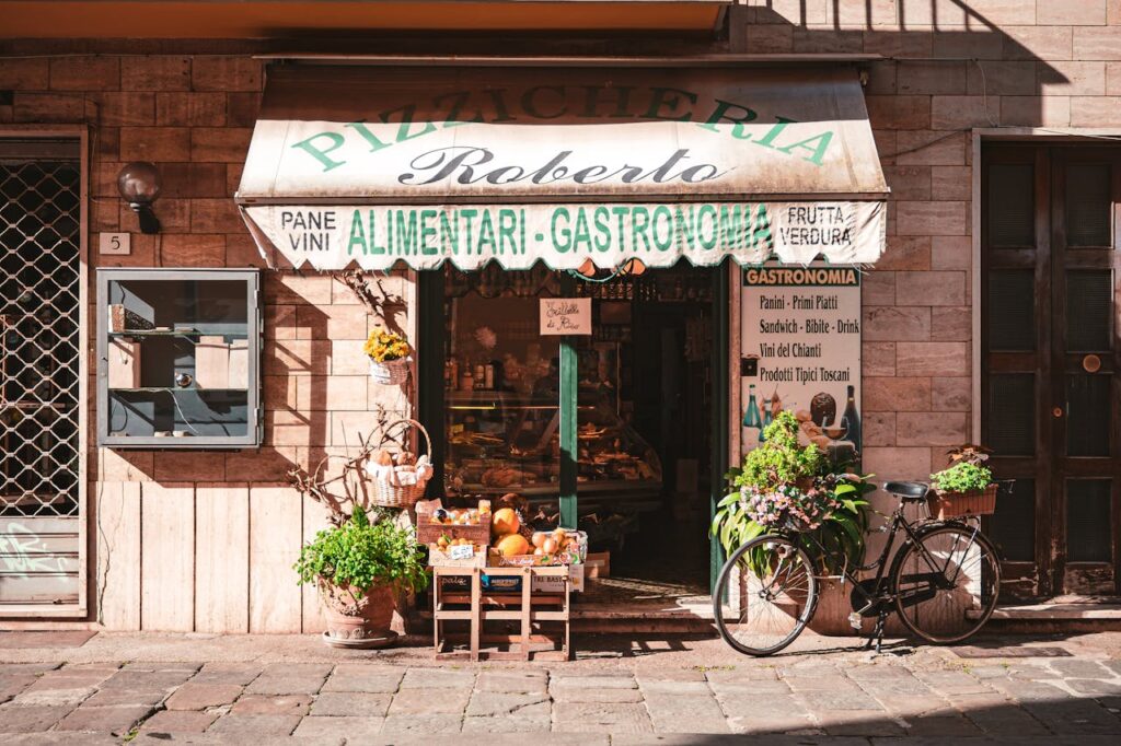 Fachada de uma pizzaria e mercearia italiana com letreiros destacando produtos alimentares.