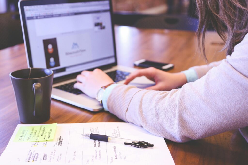 homem trabalhando em um notebook com relatórios e caneca.