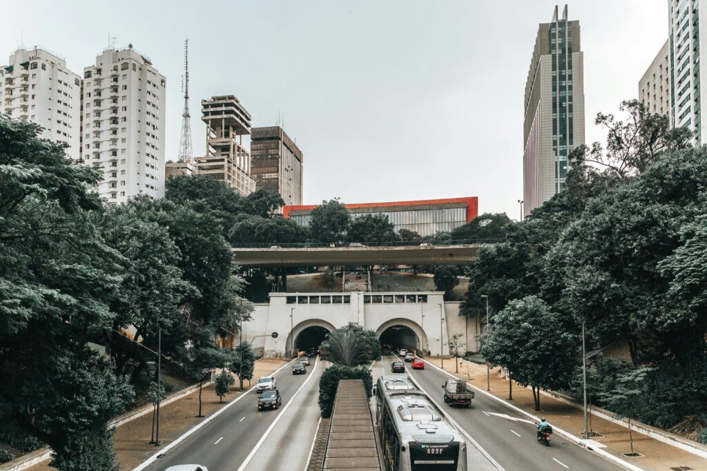 Por que empresas de transporte devem investir na comunicação em concessões públicas 3 Vista frontal da Avenida 9 de Julho, em São Paulo, com veículos circulando em ambas as direções. Ao fundo, vê-se o icônico prédio vermelho do MASP (Museu de Arte de São Paulo) sobre o viaduto da Avenida Paulista. A cena é cercada por árvores e edifícios altos, compondo o contraste entre natureza e urbanização característico da capital paulista.
