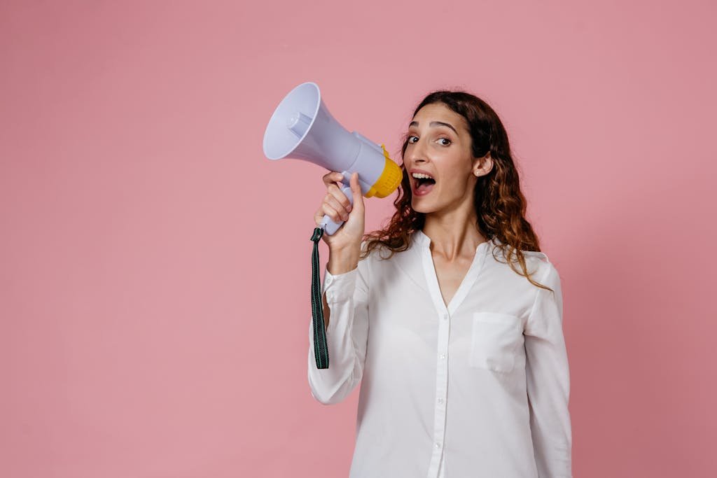 Como o marketing pode impulsionar projetos de infraestrutura urbana 6 Woman in white shirt holding megaphone against a pink background, confidently speaking.