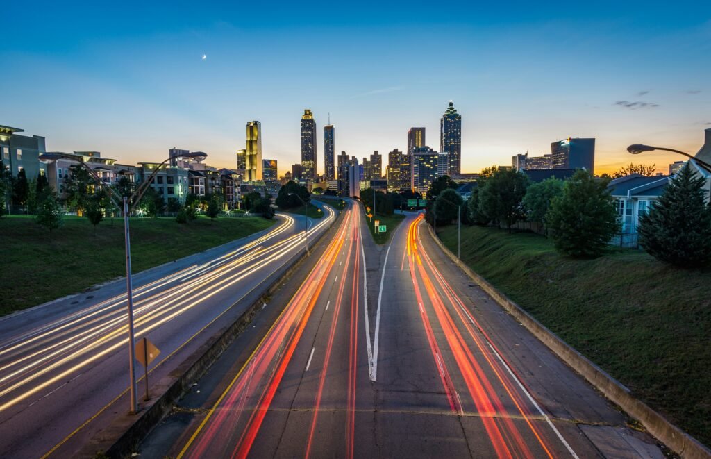 Marketing Digital para Transportadoras: o que é e como começar 2 Vista noturna de uma rodovia movimentada em direção a um centro urbano iluminado, representando fluxo logístico e infraestrutura de transporte.