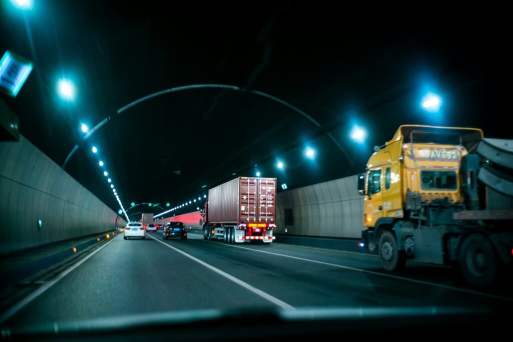 Como otimizar a captação de fretes para transportadoras 4 Caminhão transportando contêiner em túnel rodoviário iluminado à noite.