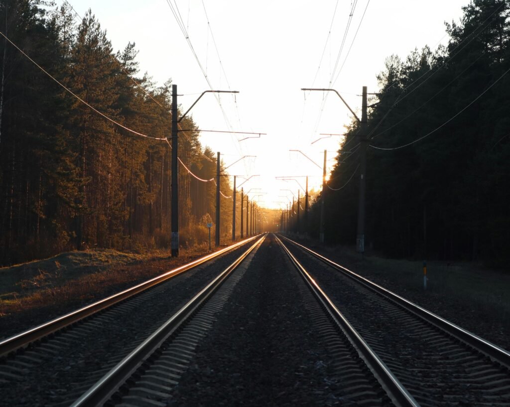 Quais são os tipos de sinalização ferroviária existentes? 5 Trilhos de trem se estendendo ao horizonte durante o pôr do sol, ladeados por árvores douradas de outono e postes de energia elétrica com cabos suspensos, criando uma perspectiva linear dramática com luz dourada.