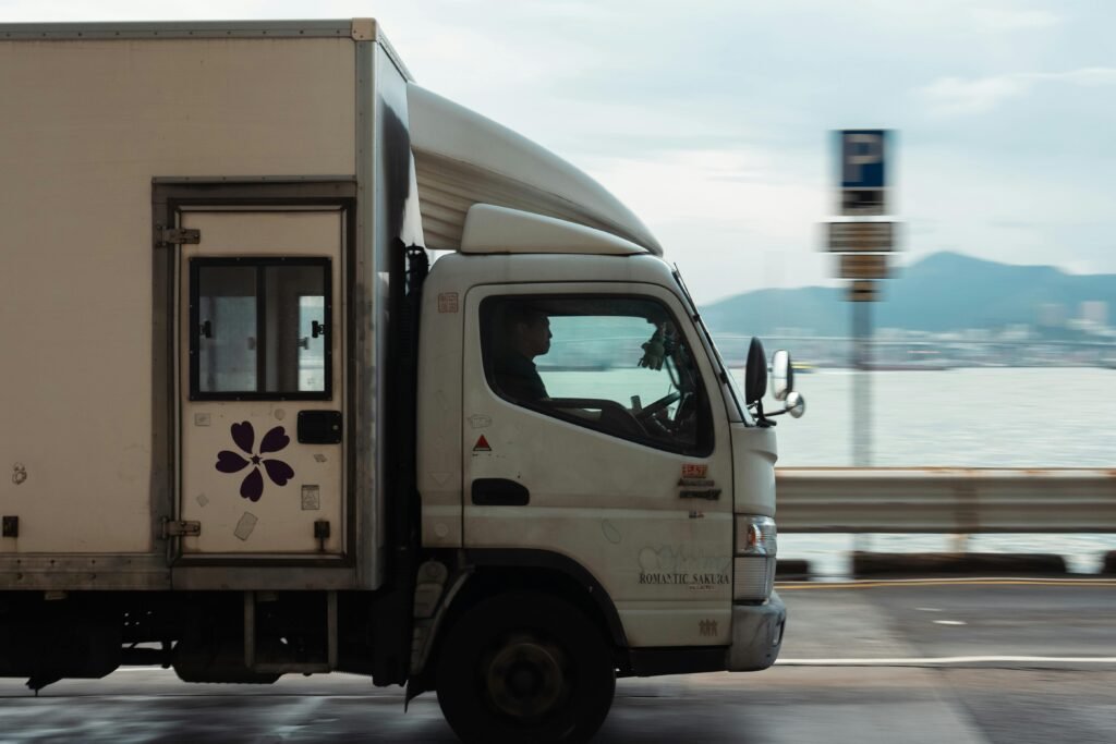 Como otimizar a captação de fretes para transportadoras 3 Caminhão branco de médio porte em movimento na estrada próximo ao litoral.