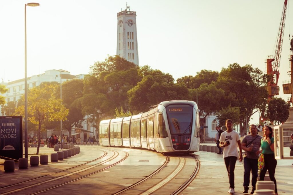 Como aplicar marketing de conteúdo para empresas de transportes 5 VLT branco circulando em uma praça urbana com pedestres durante o pôr do sol. A mobilidade urbana e o transporte de passageiros também se beneficiam do marketing de conteúdo para empresas de transportes.