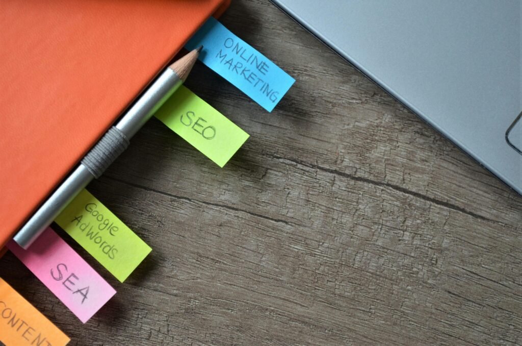 Caderno de marketing digital com anotações de SEO, Google Ads e campanhas online ao lado de notebook sobre mesa de trabalho