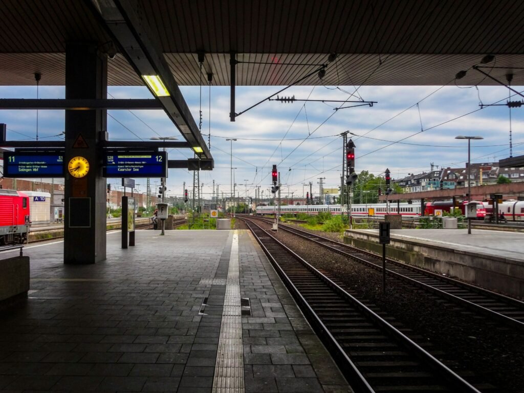 Plataforma de estação de trem com relógio amarelo, painéis de partidas e trilhos, ilustrando lições de comunicação empresarial