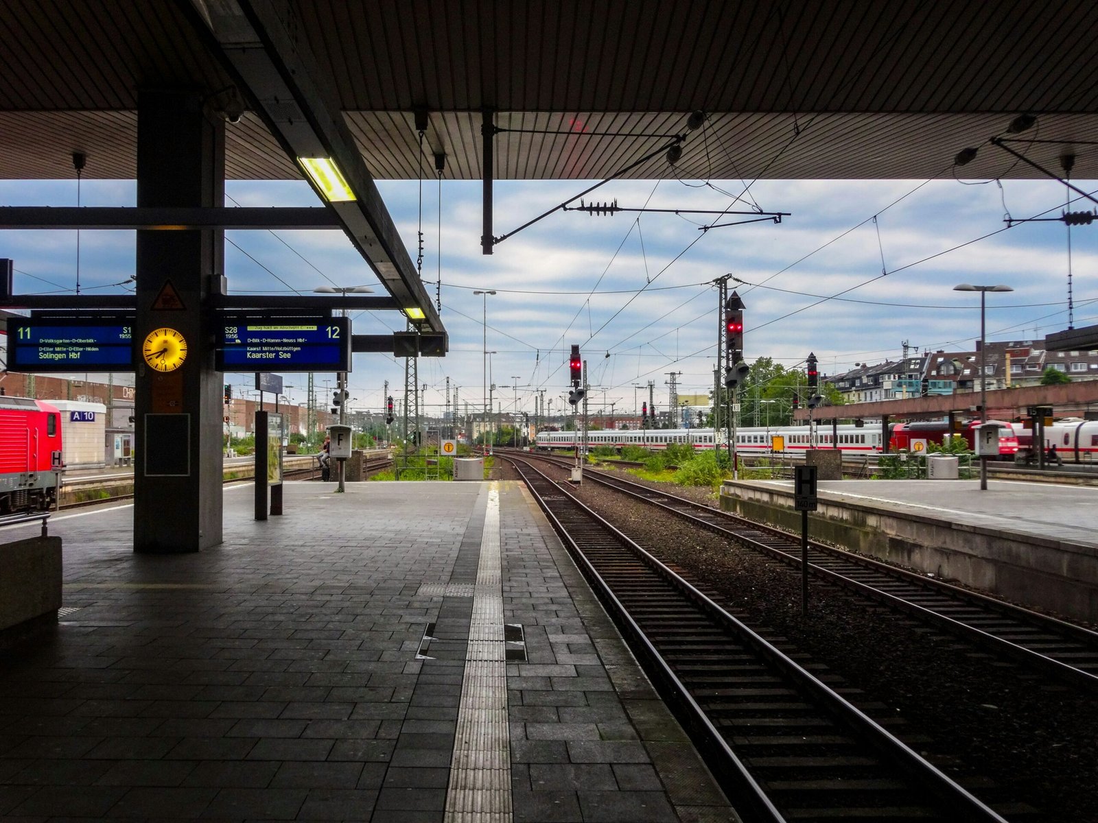 Plataforma de estação de trem com relógio amarelo, painéis de partidas e trilhos, ilustrando lições de comunicação empresarial